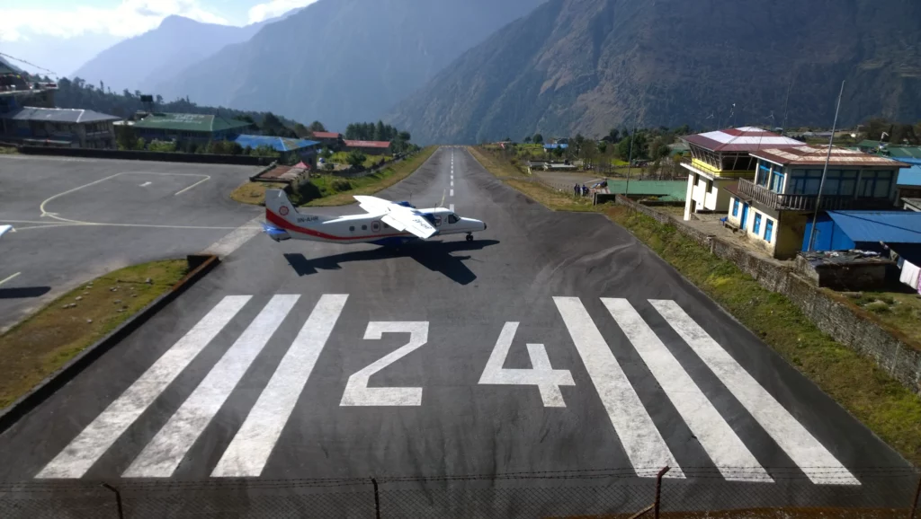 An aerial view of Lukla Airport, nestled in the mountains, with a small plane on the runway ready for takeoff.