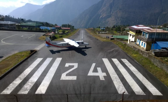 An aerial view of Lukla Airport, nestled in the mountains, with a small plane on the runway ready for takeoff.