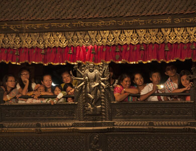 Newar family looking out from window, showcasing traditional attire and architectural details.