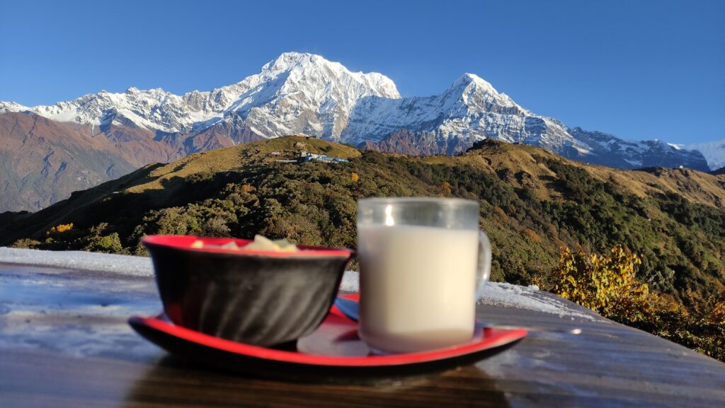 Delicious breakfast with oats, hot milk, and fruits served with a backdrop of scenic mountain vistas, combining nourishment with natural beauty.