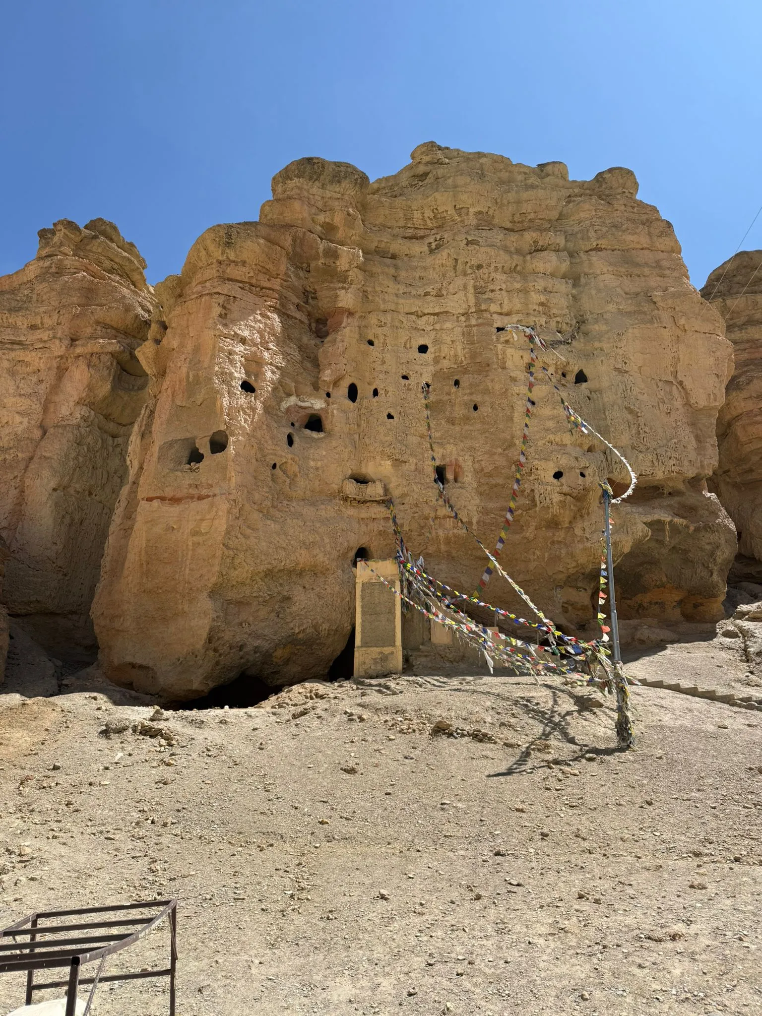 Ancient cliff caves and rock formations in Upper Mustang, Nepal, decorated with colorful Tibetan prayer flags under a clear blue sky.