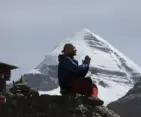 Pilgrim meditating in prayer posture with the sacred snow-covered Mount Kailash in the background during the Kailash Mansarovar Yatra.