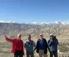 Group of trekkers standing in the scenic Upper Mustang region with snow-capped Himalayan mountains and rugged desert landscapes in the background.