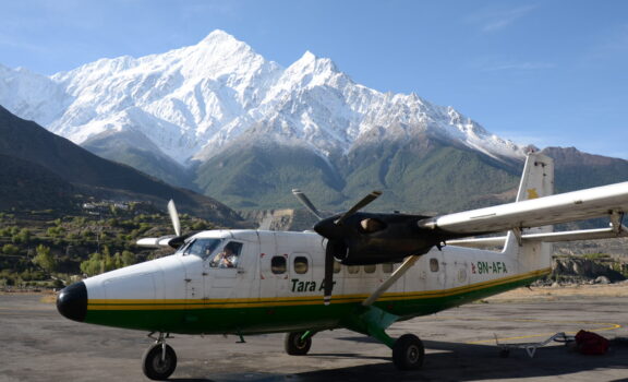 Small aircraft parked on the runway at Jomsom Airport with mountain views in the background.