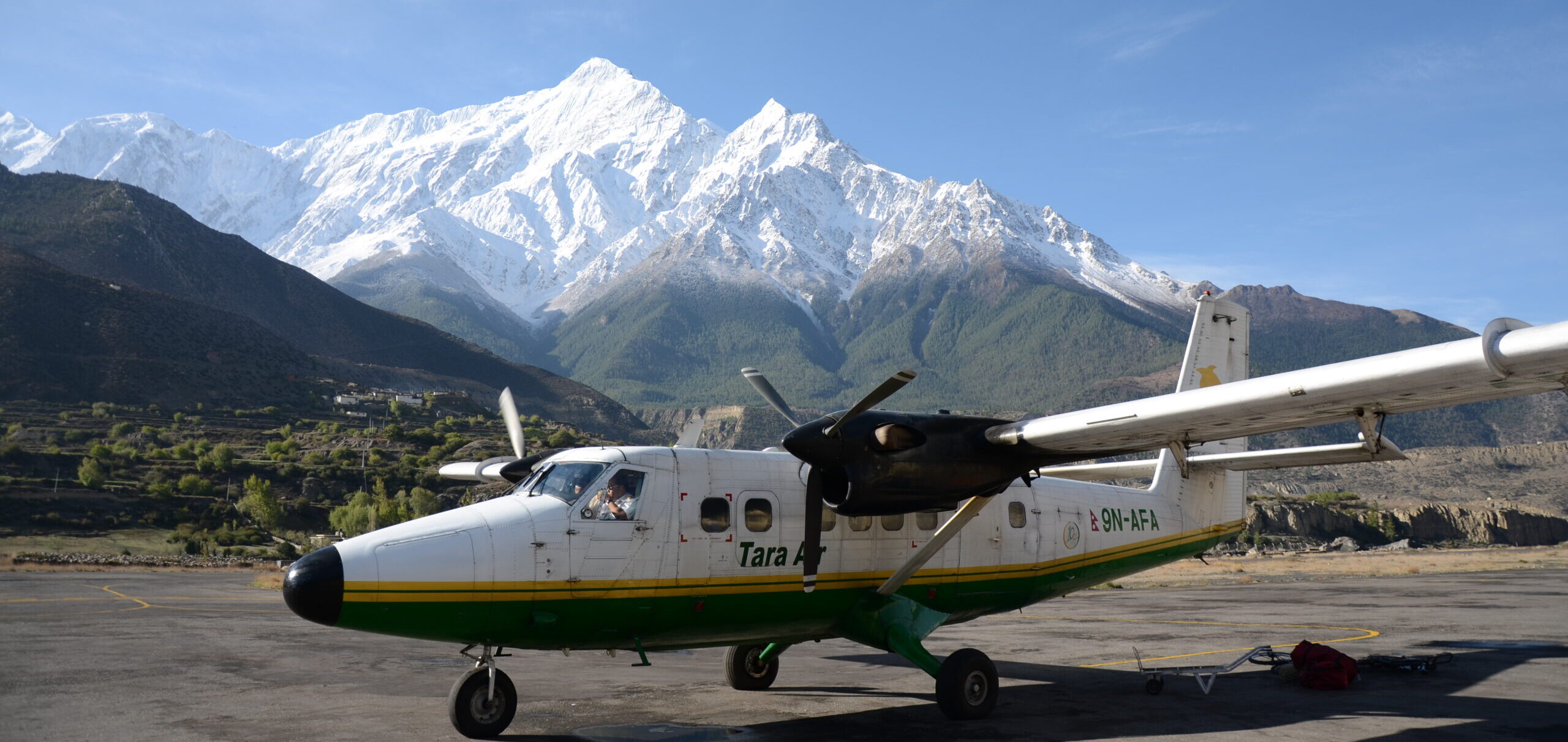 Small aircraft parked on the runway at Jomsom Airport with mountain views in the background.