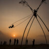 A traditional Nepali bamboo swing (ping) set up in a rural area during the Dashain and Tihar festival, with children joyfully swinging high. The swing represents spiritual cleansing and the excitement of the festive season, as villagers gather to celebrate."