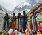 Pilgrims standing in prayer with colorful Tibetan prayer flags in front of sacred Mount Kailash during the Kailash Mansarovar Yatra in Tibet.