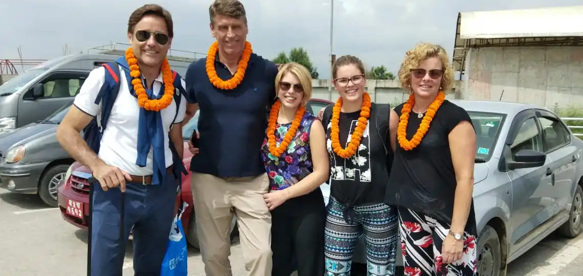 Happy international family group welcomed to Nepal with traditional marigold garlands during their Family Tour in Nepal 2026, standing together after arrival.