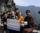 Tourists and local guides from Namaste Nepal Trekking & Research Hub posing with a Cultural Tour of Bhutan banner in front of the iconic cliffside Tiger’s Nest Monastery (Paro Taktsang), Bhutan.