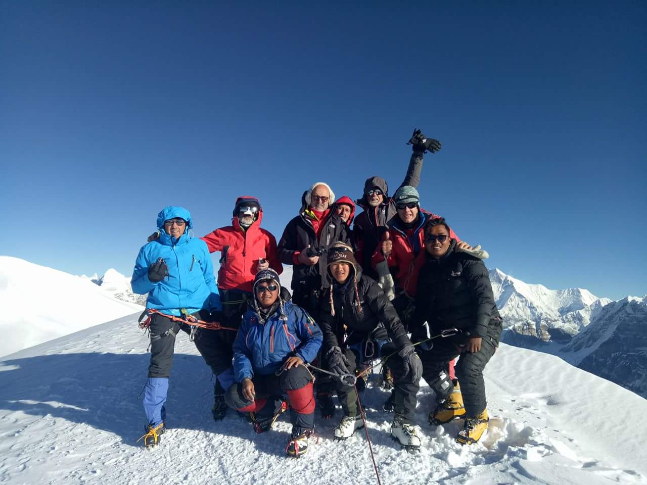 Climbing team celebrating on the summit of Mera Peak with snow-covered Himalayan peaks in Nepal